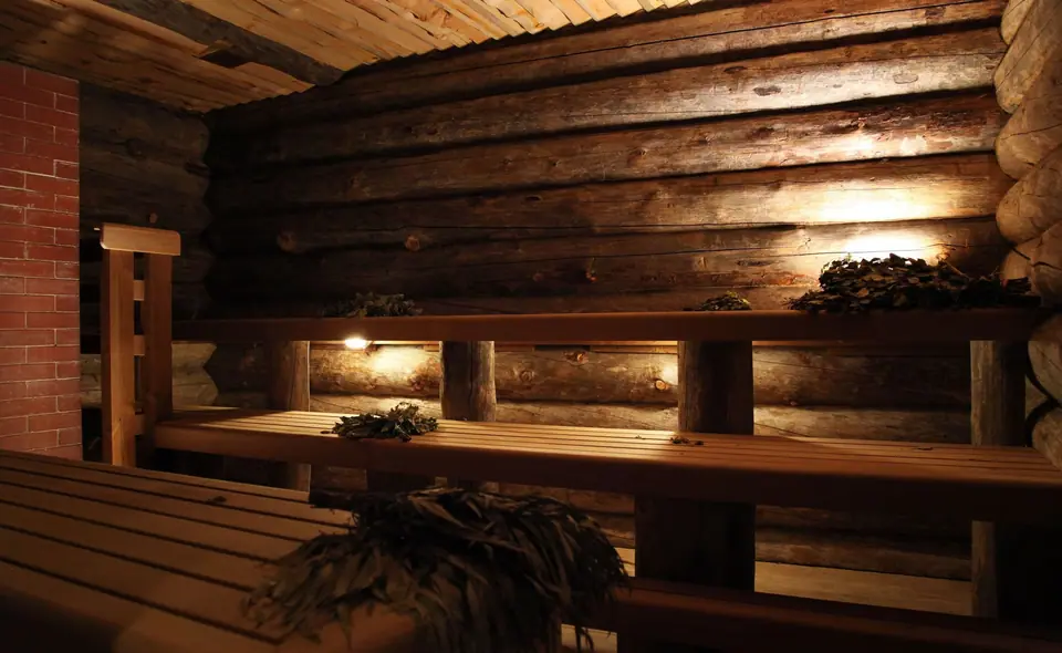 Log-walled sauna with tiered timber benches, birch venik and warm low lighting
