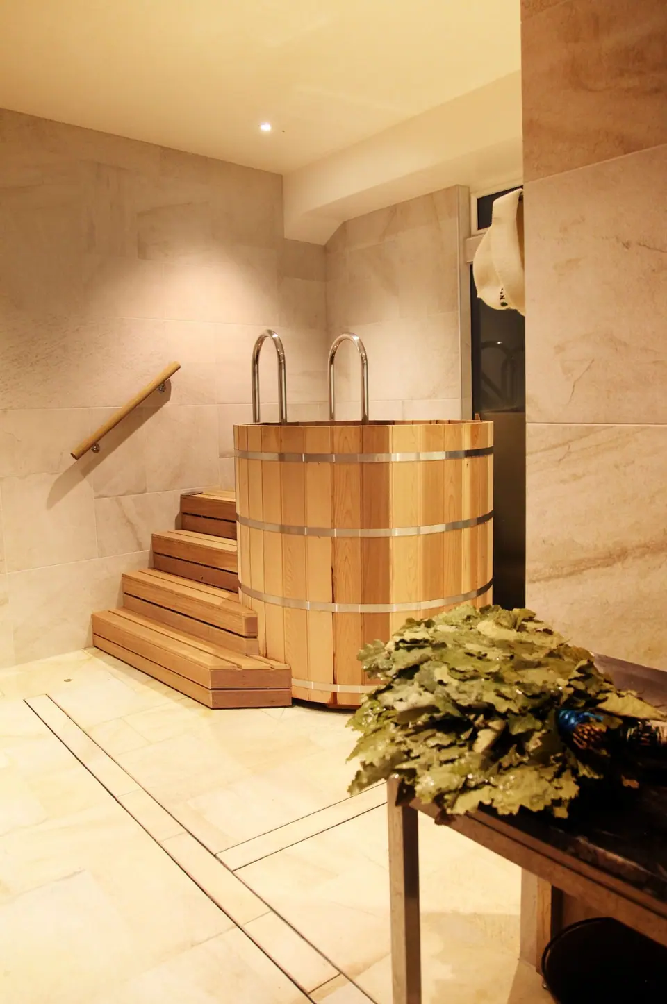 Timber plunge tub with steps, stone floor and birch branches
