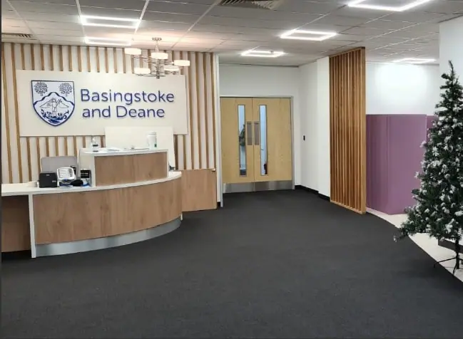 Curved timber reception desk below the Basingstoke and Deane council sign