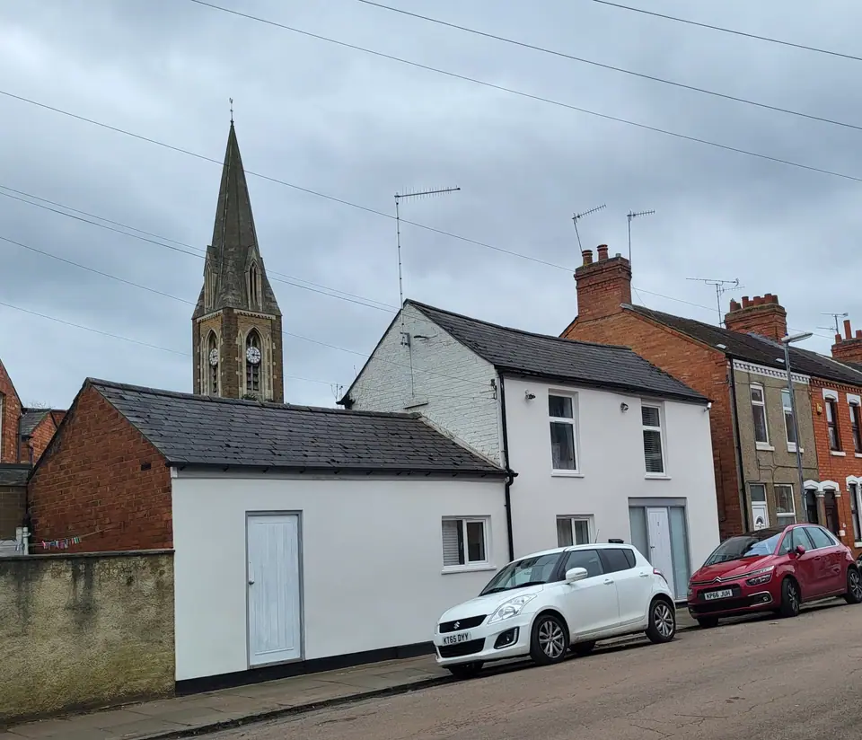 Former shop converted into a white house, with a church spire behind