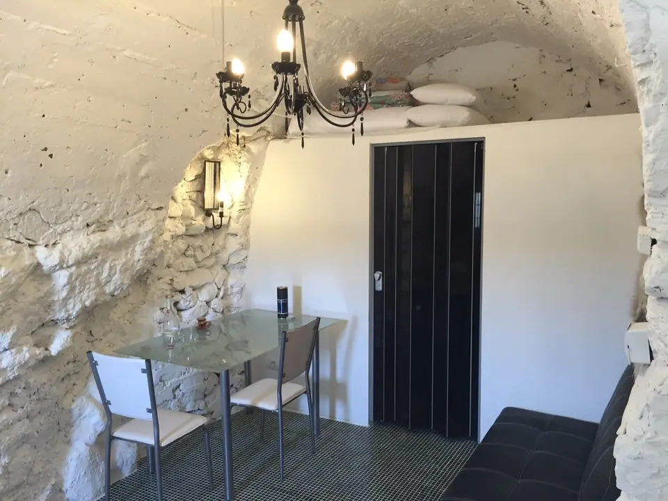 Vaulted stone studio with chandelier, glass dining table and black door