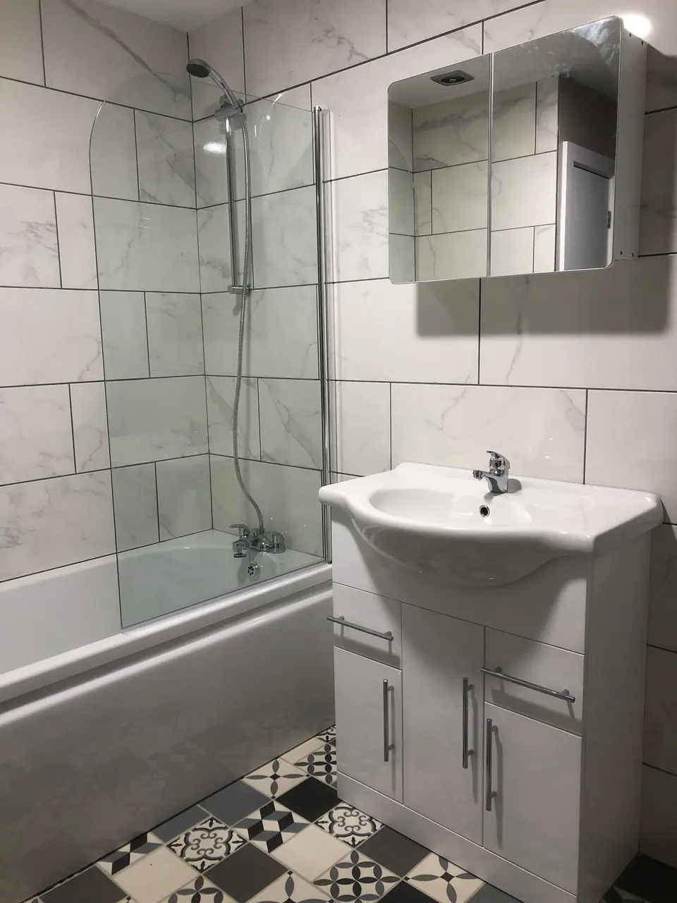 Renovated bathroom with bath, glass screen, white vanity and patterned floor tiles
