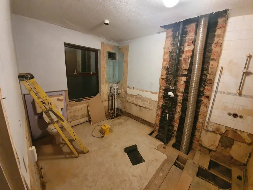 Stripped bathroom with exposed soil stack and floorboards