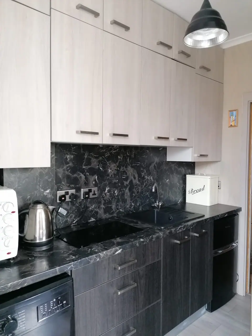 New kitchen with pale wood-effect units, black marble splashback and industrial pendant