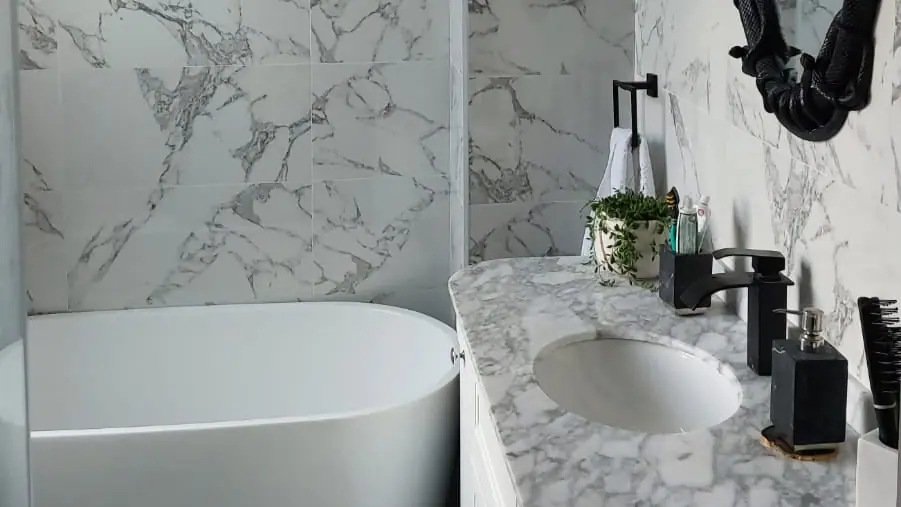 Marble-effect vanity with black tap beside a white freestanding bath